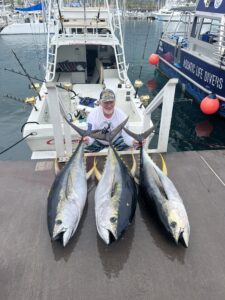 A person on the boat standing behind three large caught fish
